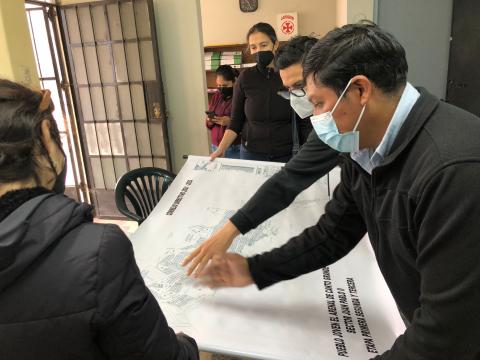 Researchers wearing masks and discussing a large blueprint