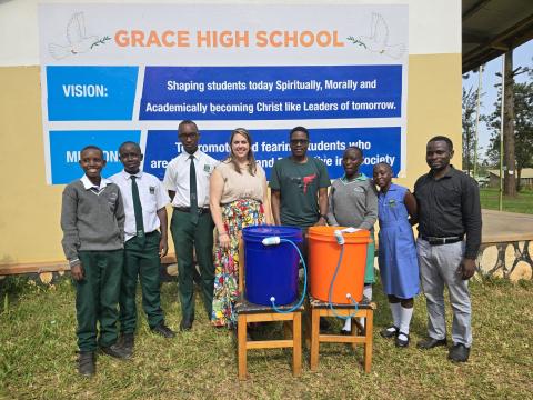 Two researchers and six Grace High School students and staff pose outside with a WASH system
